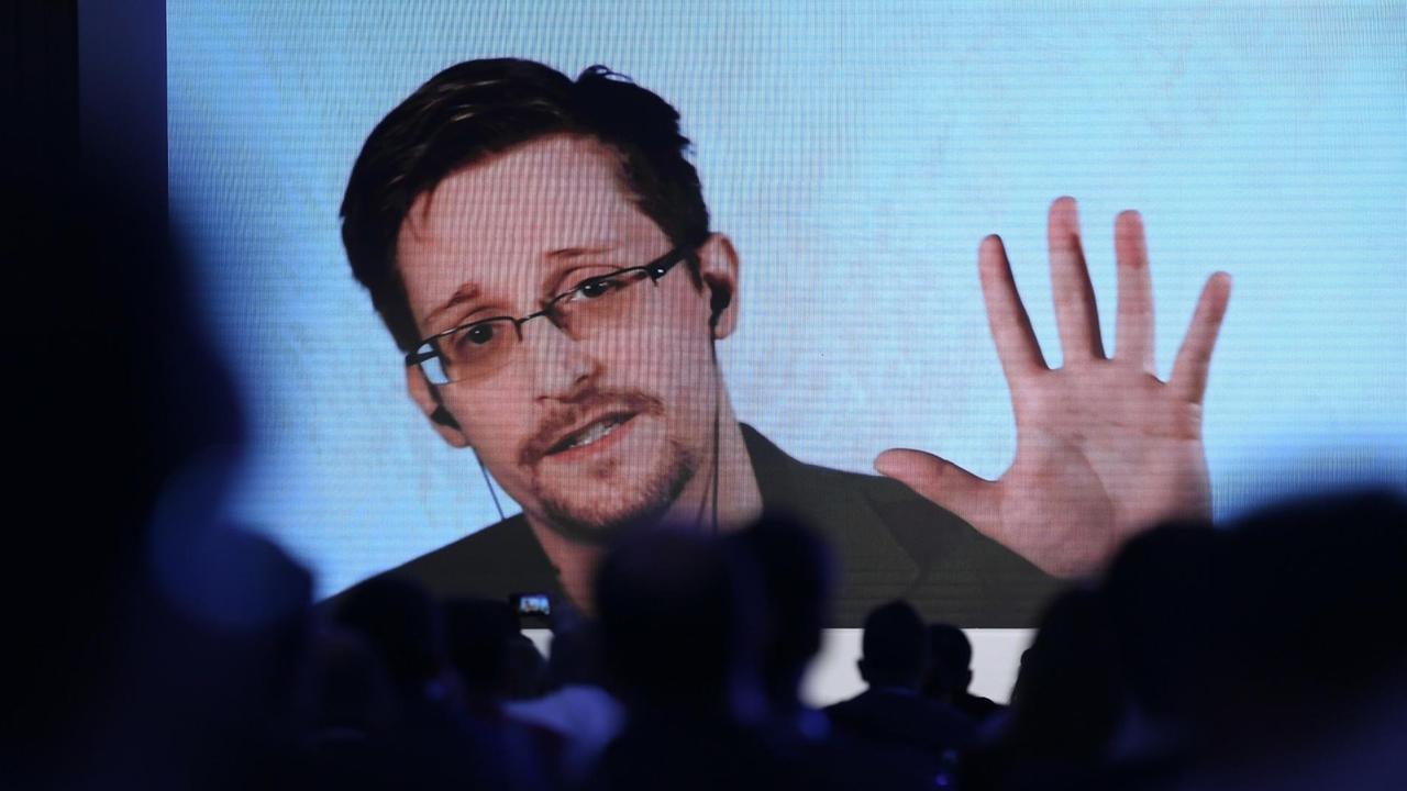 Über verschatteten Sitzreihen scheint ein auf die Bühne projizierter Stream auf, über den Edward Snowden an einer Konferenz teilnimmt. Über verschatteten Sitzreihen scheint ein auf die Bühne projizierter Stream auf, über den Edward Snowden an einer Konferenz teilnimmt.