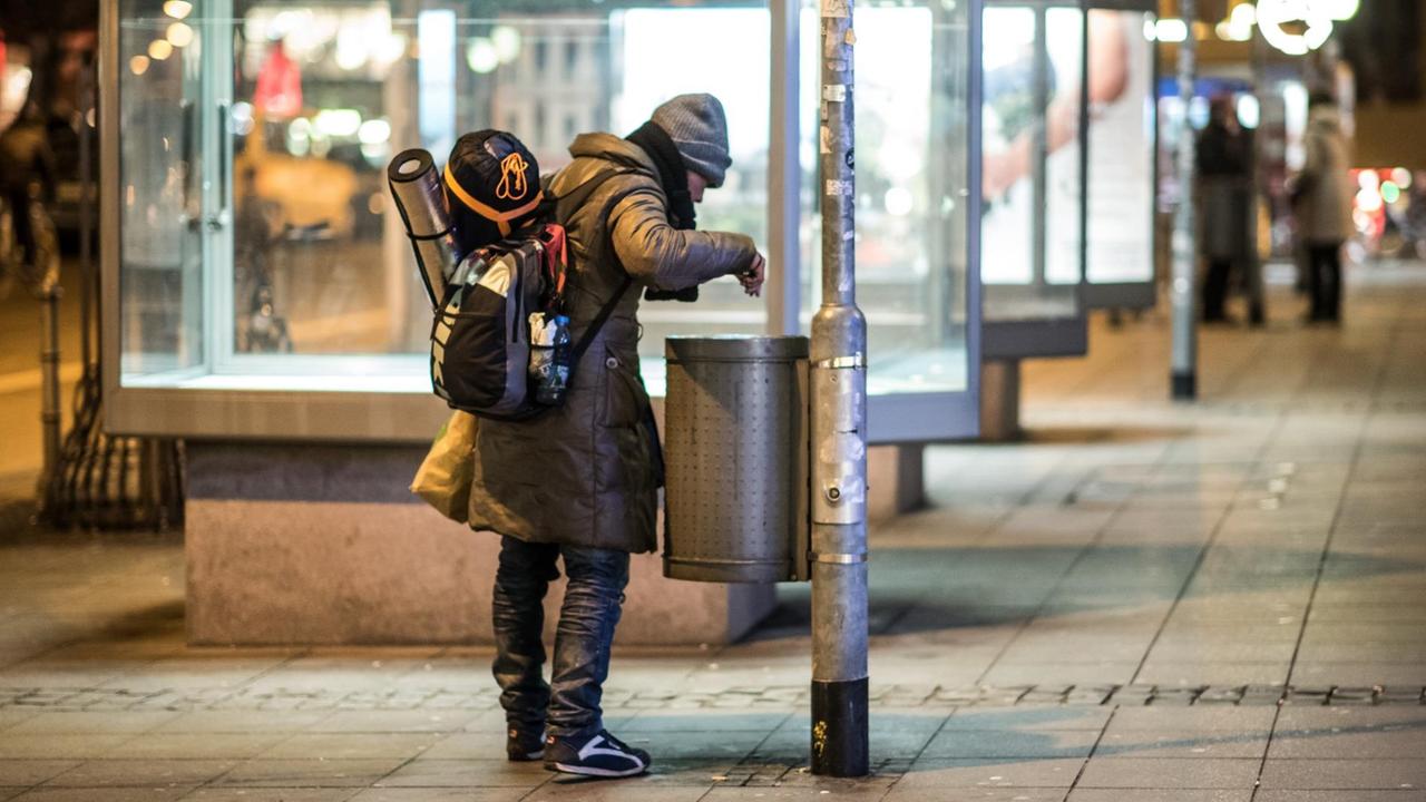 Hessen, Frankfurt am Main: Ein Obdachloser sucht mit einer Taschenlampe in einem Mülleimer nach Pfandflaschen.