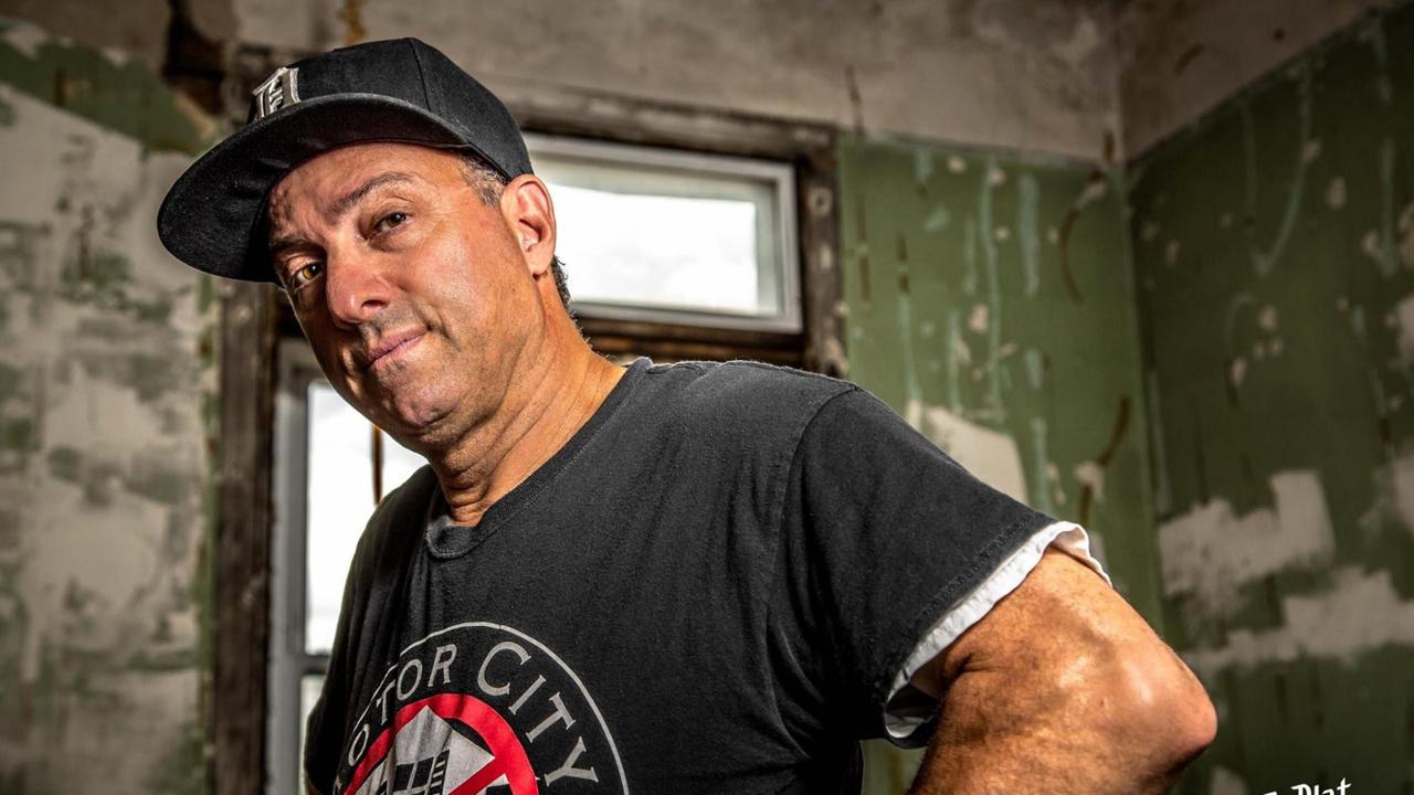 Ein Mann mit Baseballkäppi schaut stehend aufmerksam leicht schräg in die Kamera. Auf seinem schwarzen T-Shirt steht in Großbuchstaben "Motor City". Ein Mann mit Baseballkäppi schaut stehend aufmerksam leicht schräg in die Kamera. Auf seinem schwarzen T-Shirt steht in Großbuchstaben "Motor City".