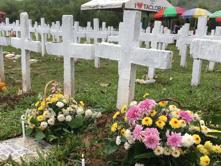 Zu sehen sind Gräber derjenigen, die beim Taifun Haiyan ums Leben kamen. Es sind weiße Kreuze zu sehen und bunte Blumen.