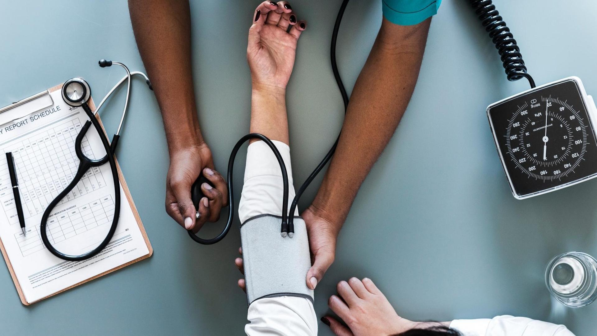 Eine Pflegekraft misst den Blutdruck eines Patienten. Von beiden sind nur die Hände und Arme zu sehen. Eine Pflegekraft misst den Blutdruck eines Patienten. Von beiden sind nur die Hände und Arme zu sehen.
