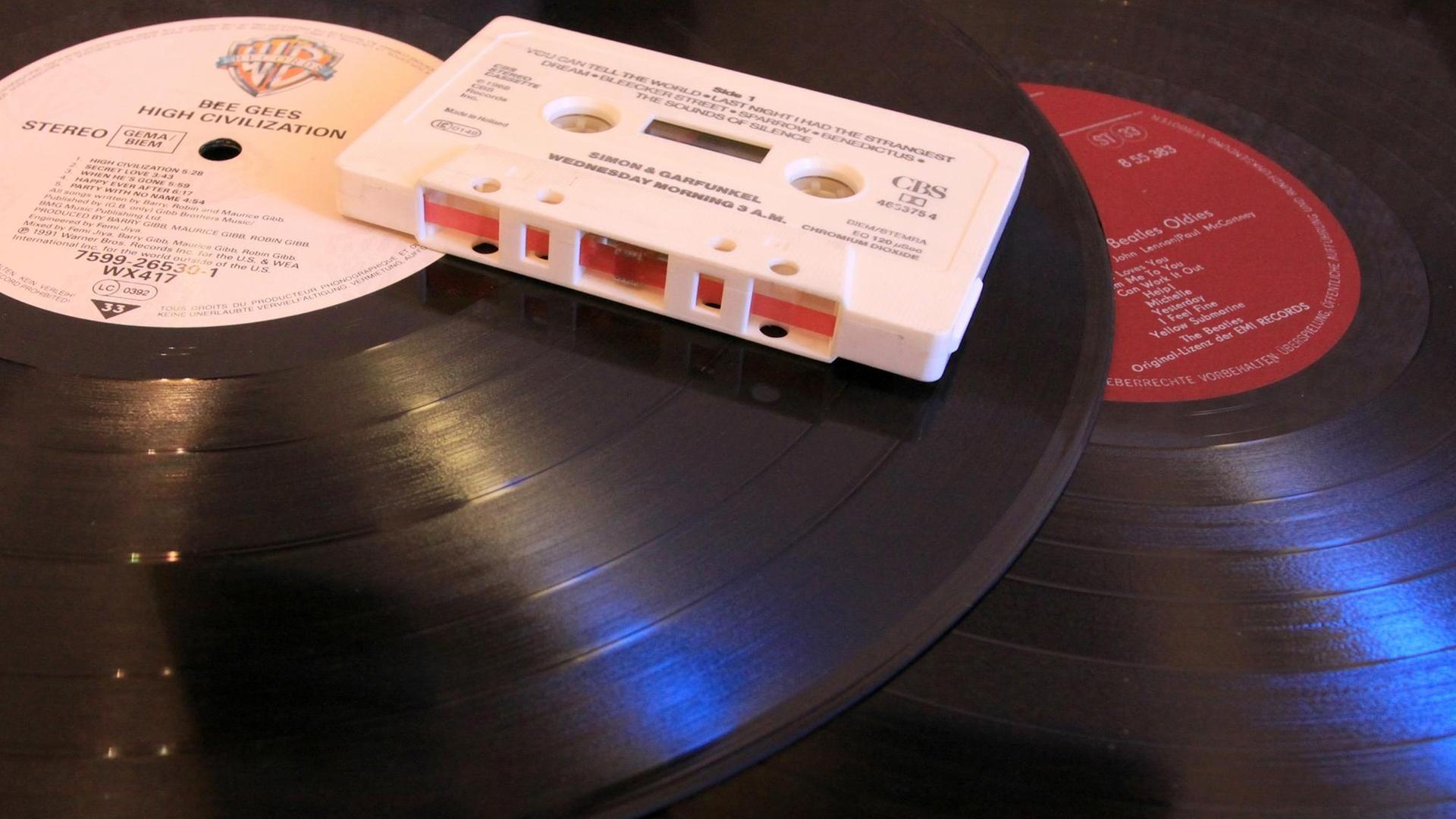 ILLUSTRATION - Eine Audio-Kompaktkassette (Musikkassette, MC, Audiokassette) liegt am 12.12.2014 in Berlin auf zwei Vinyl-Schallplatten (Langspielplatten, LP). Die mit einem Magnetband ausgerüstete Kassette, die in den 1970er Jahren bis in die 1990er Jahre hinein weit verbreitet war, wurde in einem Kassettenrekorder abgespielt und ermöglichte erstmals den mobilen Konsum von Musik. Beide Tonträger haben mit der Einführung der digitalen Audiotechnik der CD (Kompaktdisc) an Bedeutung verloren. Foto: Peter Zimmermann | Verwendung weltweit ILLUSTRATION - Eine Audio-Kompaktkassette (Musikkassette, MC, Audiokassette) liegt am 12.12.2014 in Berlin auf zwei Vinyl-Schallplatten (Langspielplatten, LP). Die mit einem Magnetband ausgerüstete Kassette, die in den 1970er Jahren bis in die 1990er Jahre hinein weit verbreitet war, wurde in einem Kassettenrekorder abgespielt und ermöglichte erstmals den mobilen Konsum von Musik. Beide Tonträger haben mit der Einführung der digitalen Audiotechnik der CD (Kompaktdisc) an Bedeutung verloren. Foto: Peter Zimmermann | Verwendung weltweit
