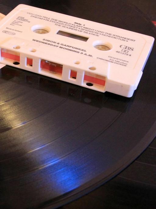 ILLUSTRATION - Eine Audio-Kompaktkassette (Musikkassette, MC, Audiokassette) liegt am 12.12.2014 in Berlin auf zwei Vinyl-Schallplatten (Langspielplatten, LP). Die mit einem Magnetband ausgerüstete Kassette, die in den 1970er Jahren bis in die 1990er Jahre hinein weit verbreitet war, wurde in einem Kassettenrekorder abgespielt und ermöglichte erstmals den mobilen Konsum von Musik. Beide Tonträger haben mit der Einführung der digitalen Audiotechnik der CD (Kompaktdisc) an Bedeutung verloren. Foto: Peter Zimmermann | Verwendung weltweit