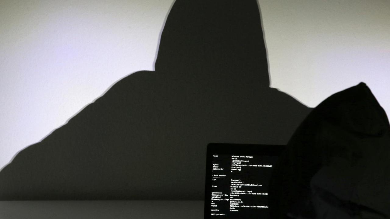 Hinter einem Laptop wird der Schatten eines Mannes an die Wand geworfen.