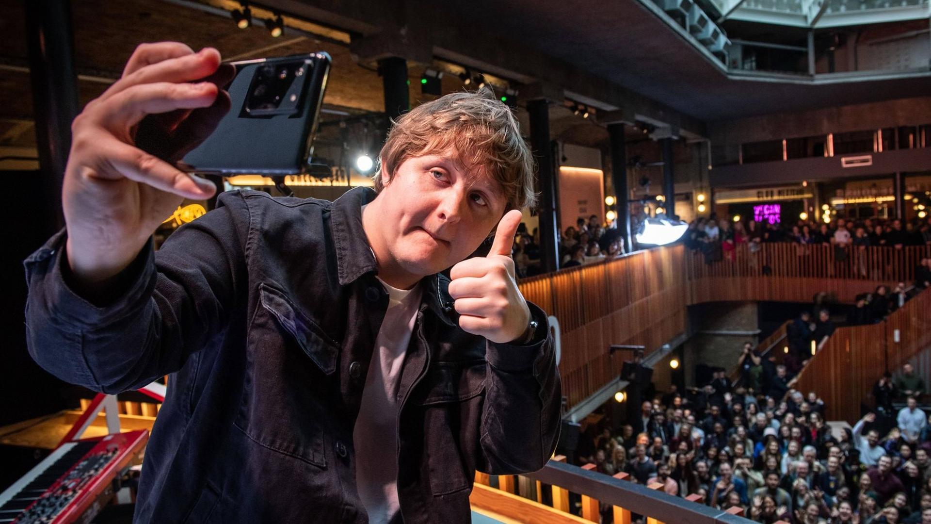 Lewis Capaldi macht ein Selfie von sich mit den Zuschauern und hebt dabei den Daumen hoch Lewis Capaldi macht ein Selfie von sich mit den Zuschauern und hebt dabei den Daumen hoch