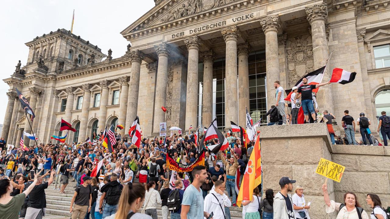eilnehmer einer Kundgebung gegen die Corona-Maßnahmen stehen auf den Stufen zum Reichstagsgebäude, zahlreiche Reichsflaggen sind zu sehen.