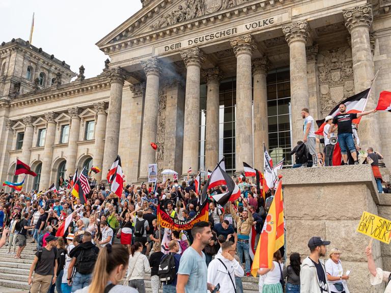 Teilnehmer einer Kundgebung gegen die Corona-Maßnahmen stehen auf den Stufen zum Reichstagsgebäude, zahlreiche Reichsflaggen sind zu sehen.
