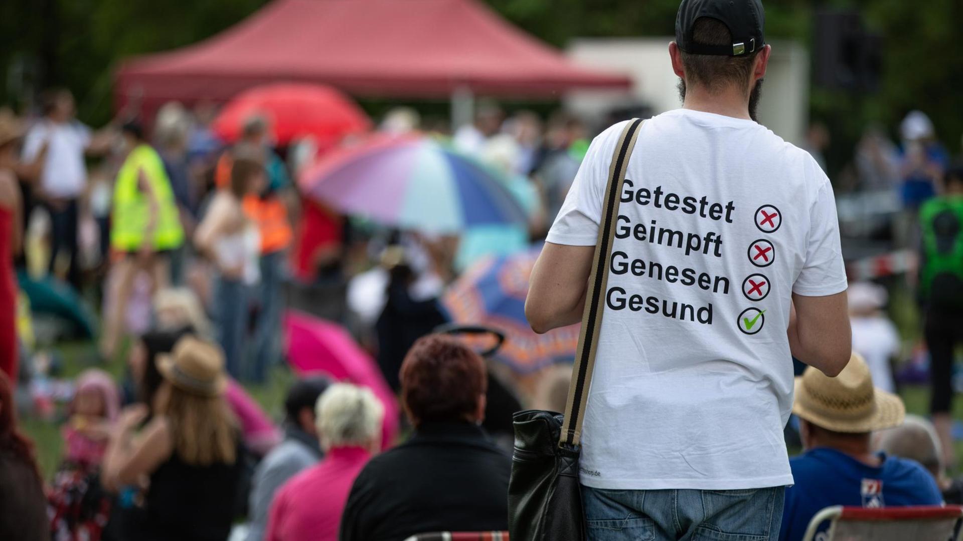 Ein Mann trägt auf einer Demonstration der Initiative „Querdenken“ ein T-Shirt mit der Aufschrift 'Getestet, Geimpft, Genesen, Gesund'".