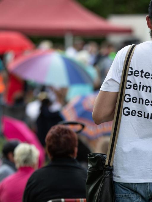 Ein Mann trägt auf einer Demonstration der Initiative „Querdenken“ ein T-Shirt mit der Aufschrift 'Getestet, Geimpft, Genesen, Gesund'".