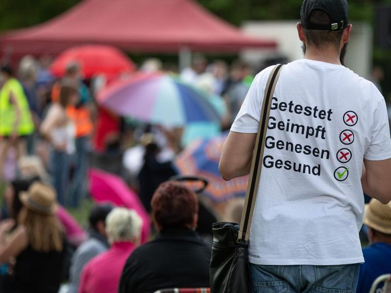 Ein Mann trägt auf einer Demonstration der Initiative „Querdenken“ ein T-Shirt mit der Aufschrift 'Getestet, Geimpft, Genesen, Gesund'".