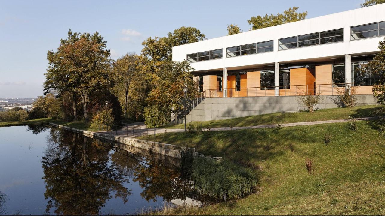Ein heller Neubau steht am Ufer eines Sees. Ein heller Neubau steht am Ufer eines Sees.