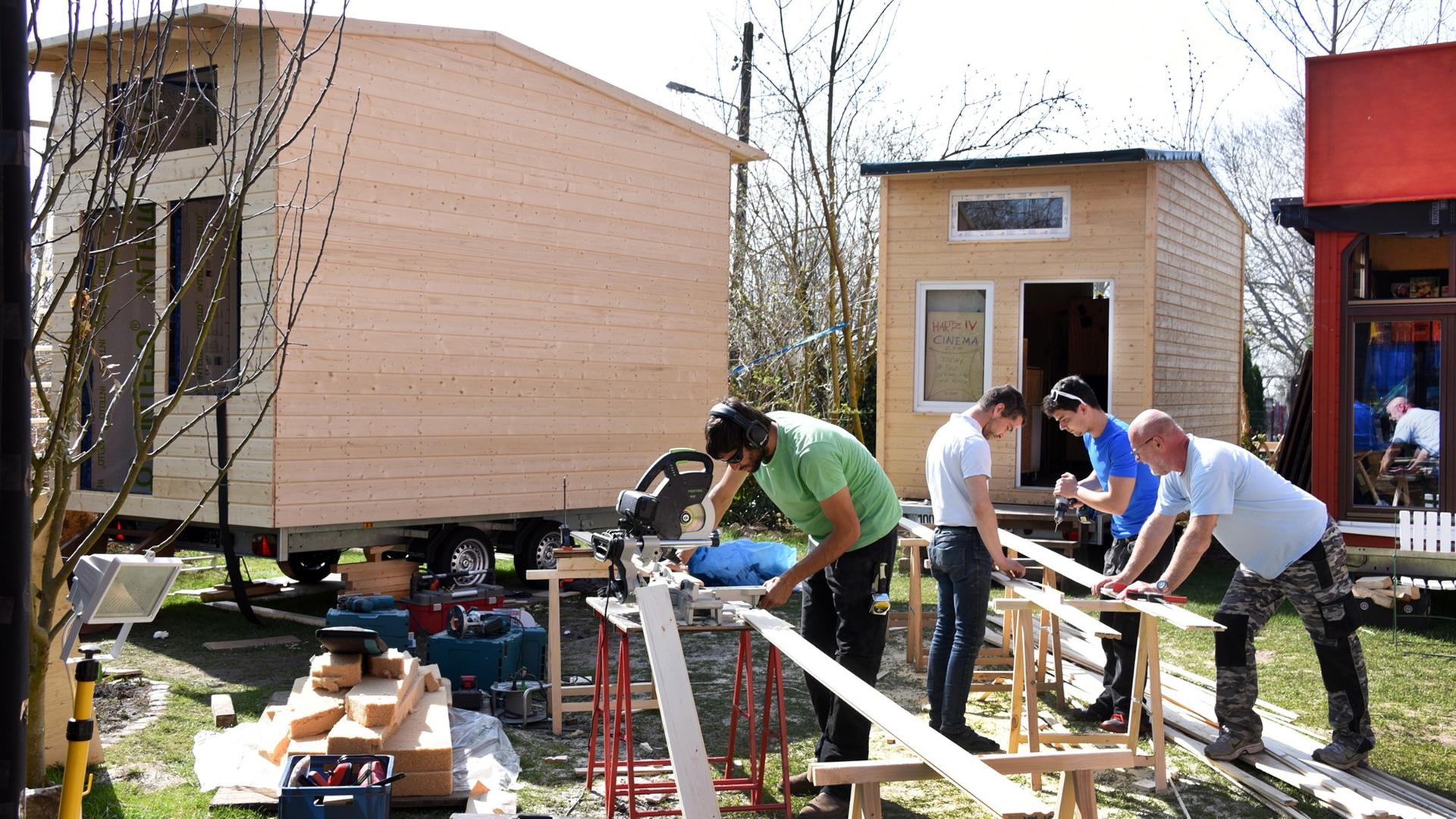 Mehrere Personen arbeiten in Wittenberg im Garten vom Cranach-Haus an Tiny-Häusern, die zu einem temporären Dorf aus Mikrowohnungen gehören. Mehrere Personen arbeiten in Wittenberg im Garten vom Cranach-Haus an Tiny-Häusern, die zu einem temporären Dorf aus Mikrowohnungen gehören.