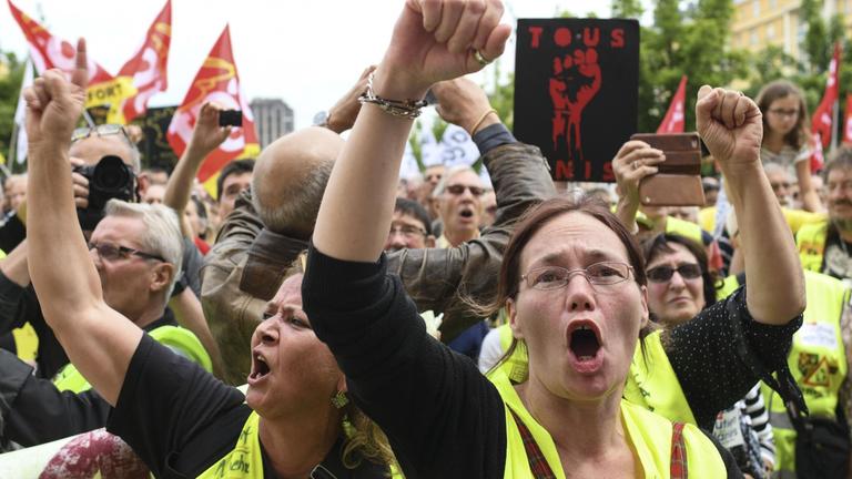 Demonstrantinnen in gelben Westen recken Fäuste in die Höhe und skandieren offenbar etwas. 