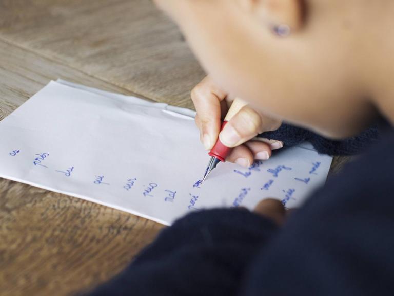 Nahaufnahme eines Kindes, das mit Füller auf Papier schreibt.