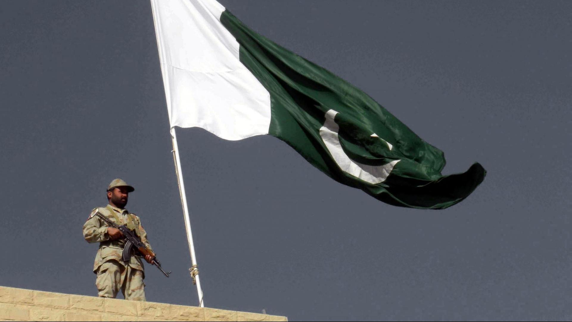 Ein Pakistanischer Soldat steht auf einer Mauer an der pakistanisch-afghanischen Grenze. Im Hintergrund weht die Pakistanische Flagge Ein Pakistanischer Soldat steht auf einer Mauer an der pakistanisch-afghanischen Grenze. Im Hintergrund weht die Pakistanische Flagge