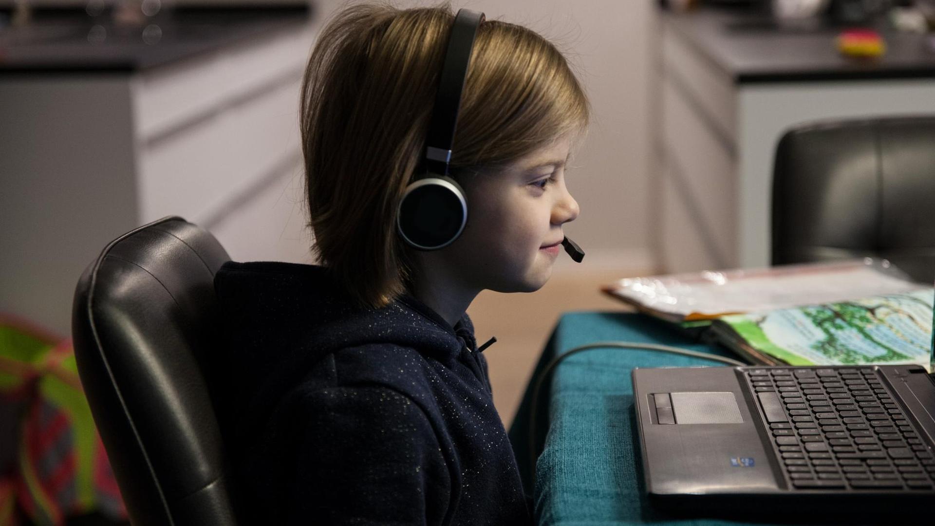 Ein Grundschulkind mit Headset sitzt im Januar 2021 an einem Tisch und macht Homeschooling. Auf dem Tisch steht ein aufgeklappter Laptop. Neben dem Laptop liegen Schulbücher auf dem Tisch. Ein Grundschulkind mit Headset sitzt im Januar 2021 an einem Tisch und macht Homeschooling. Auf dem Tisch steht ein aufgeklappter Laptop. Neben dem Laptop liegen Schulbücher auf dem Tisch.