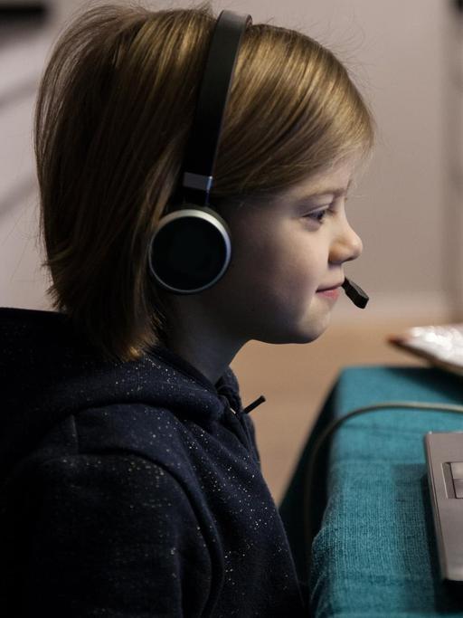Ein Grundschulkind mit Headset sitzt im Januar 2021 an einem Tisch und macht Homeschooling. Auf dem Tisch steht ein aufgeklappter Laptop. Neben dem Laptop liegen Schulbücher auf dem Tisch.
