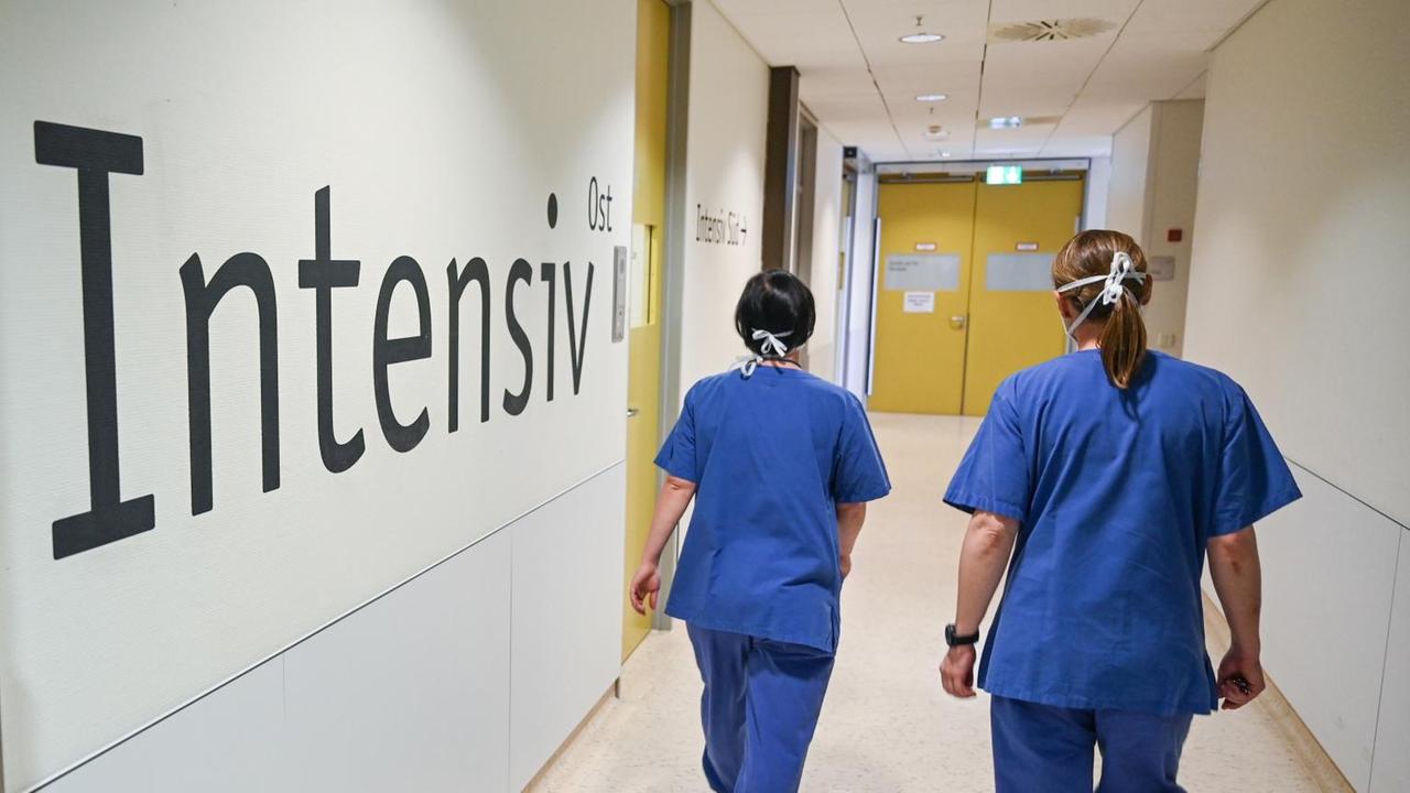 Zwei Pflegerinnen gehen durch einen Gang, an dessen Wand Intensivstation steht Zwei Pflegerinnen gehen durch einen Gang, an dessen Wand Intensivstation steht