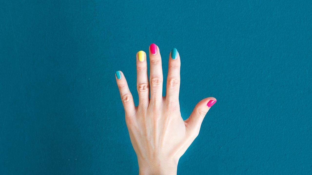 Eine Hand mit buntlackierten Fingernägeln vor blauem Hintergrund. Eine Hand mit buntlackierten Fingernägeln vor blauem Hintergrund.