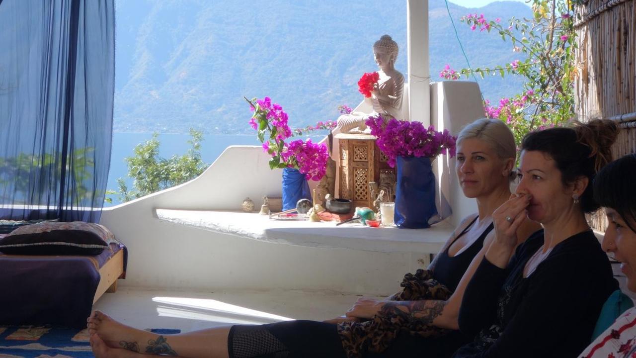 Yogalehrer und Reikimeister sitzen auf einer Terrasse am und nehmen am "Mayan Abdominal Massage"-Kurs teil. Im Hinterggrund ist der Vulkan Atitlan in Guatemala zu sehen. Yogalehrer und Reikimeister sitzen auf einer Terrasse am und nehmen am "Mayan Abdominal Massage"-Kurs teil. Im Hinterggrund ist der Vulkan Atitlan in Guatemala zu sehen.