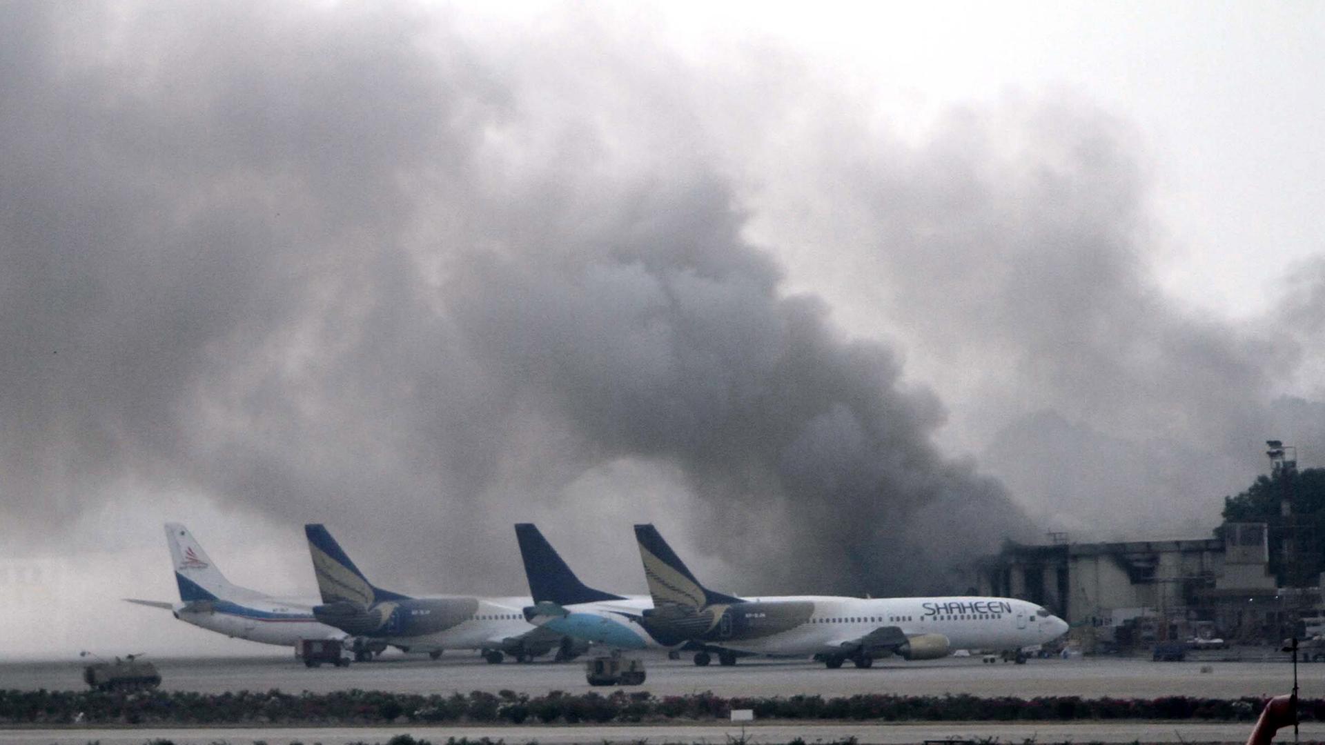 Hinter vier Flugzeugen ist ein qualmendes Gebäude zu sehen.