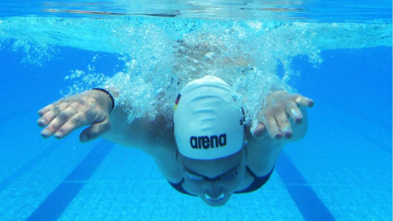 Eine Sportschwimmerin taucht mit weißer Badekappe ins lichtblaue Wasser. Eine Sportschwimmerin taucht mit weißer Badekappe ins lichtblaue Wasser.