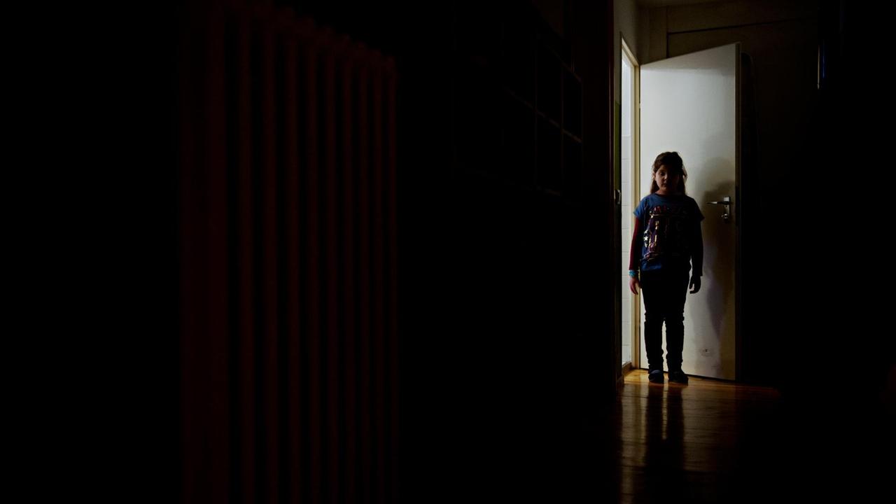 ILLUSTRATION - Ein junges Mädchen steht am 24.01.2014 in Berlin am Ende eines dunklen Flures.