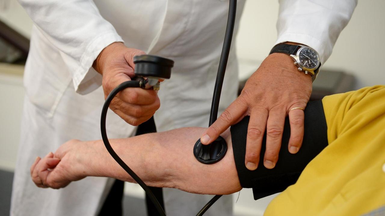 Ein Hausarzt misst in seiner Praxis einer Patientin den Blutdruck.