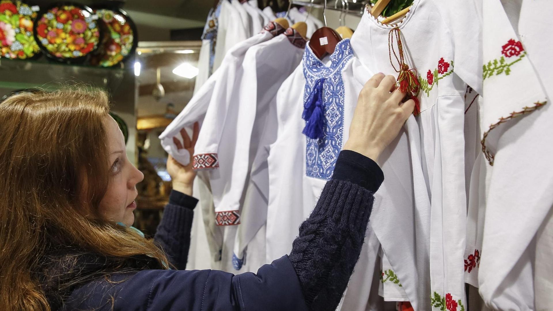 Eine Verkäuferin schaut sich Vyshyvanka Blusen mit traditionell ukrainischen Stickereien an. Eine Verkäuferin schaut sich Vyshyvanka Blusen mit traditionell ukrainischen Stickereien an.