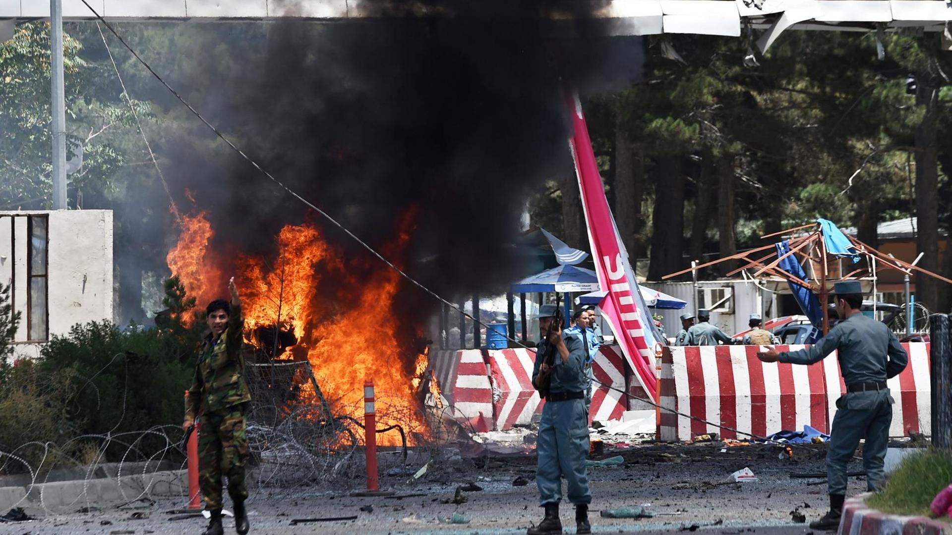 Afghanische Sicherheitskräfte vor brennenden Trümmern nach der Explosion am Kabuler Flughafen. Afghanische Sicherheitskräfte vor brennenden Trümmern nach der Explosion am Kabuler Flughafen.