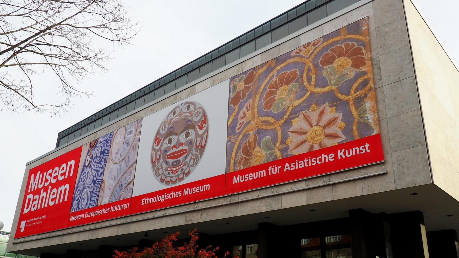 Das Gebäude der Museen Dahlem in Berlin. Ein rechteckiger Betonbau auf dem vorne drei Plakate zu sehen sind, die auf die Sammlungen im Haus verweisen: Das Museum europäischer Kulturen, das Ethnologische Museum und das Museum für Asiatische Kunst. Nur das erstgenannte befindet sich noch an diesem Standort.