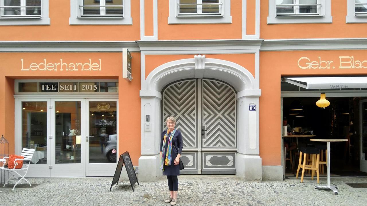Friederike Fechner steht vor der sanierten, orange farbenen Fassade des ehemaligen Hauses der Familie Blach. Friederike Fechner steht vor der sanierten, orange farbenen Fassade des ehemaligen Hauses der Familie Blach.