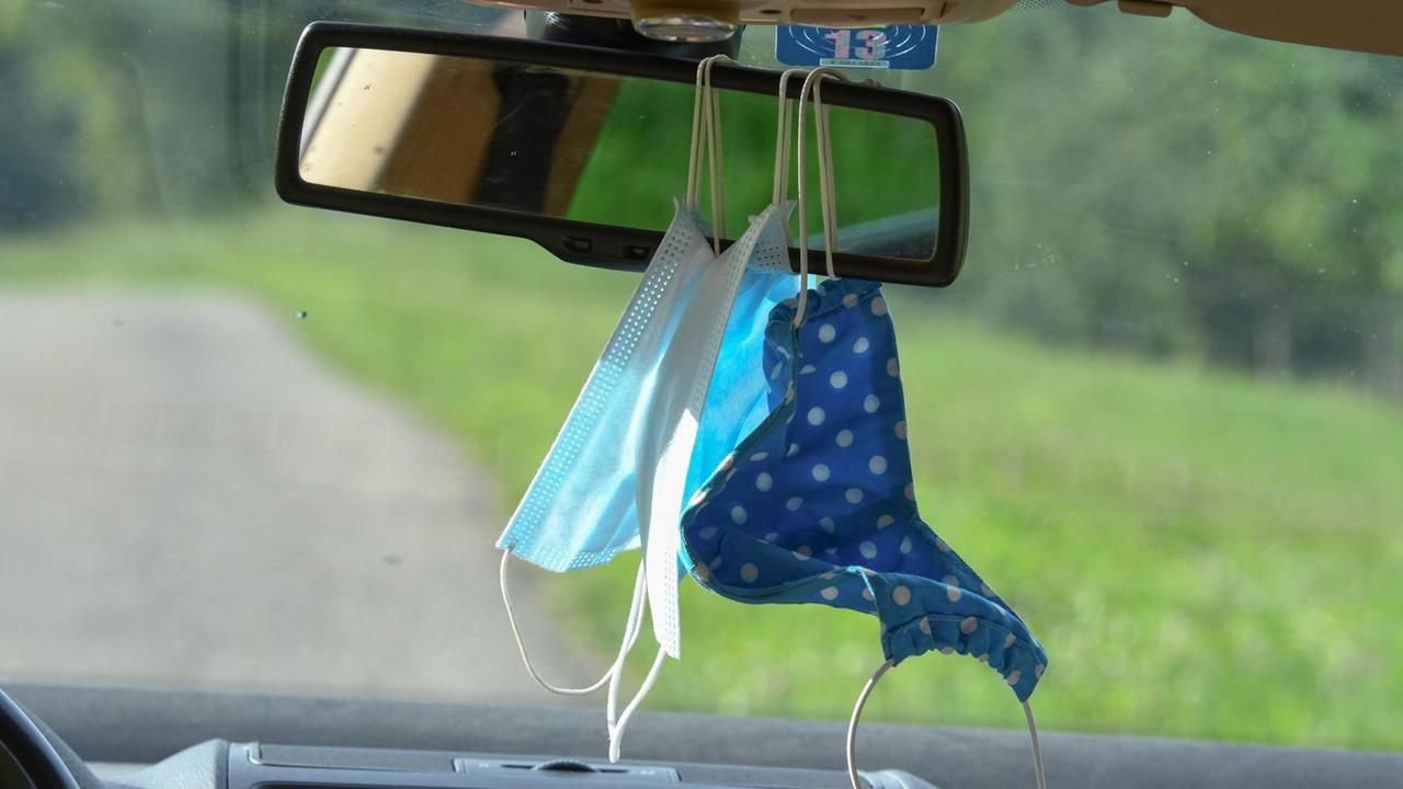 Mund-Nasenschutz-Masken hängen im Auto am Rückspiegel. Mund-Nasenschutz-Masken hängen im Auto am Rückspiegel.