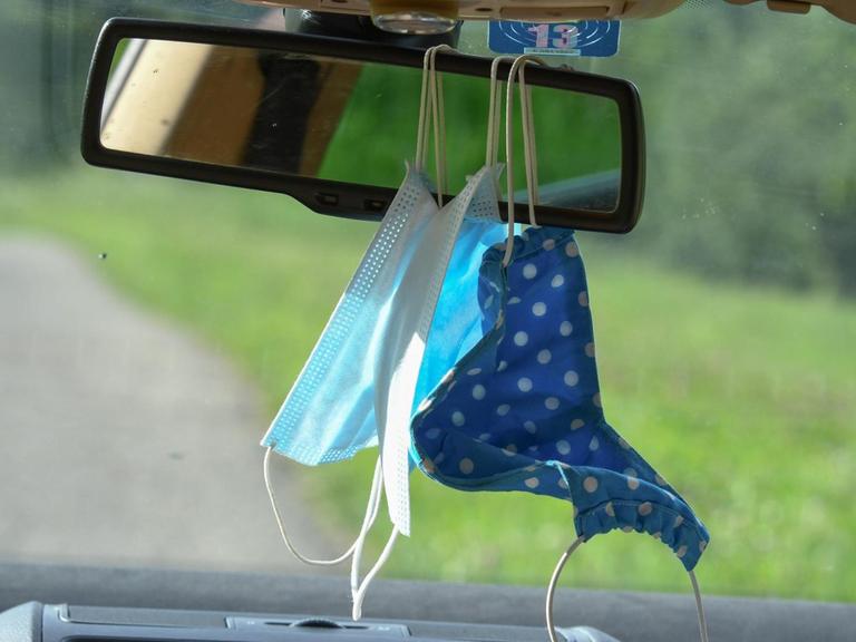 Mund-Nasenschutz-Masken hängen im Auto am Rückspiegel. 