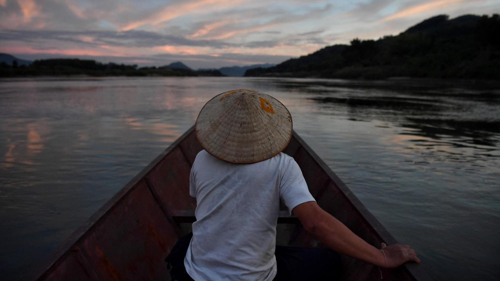 Ein Mann sitzt in einem Fischerboot und fährt in der Dämmerung den Mekong Strom entlang. Ein Mann sitzt in einem Fischerboot und fährt in der Dämmerung den Mekong Strom entlang.