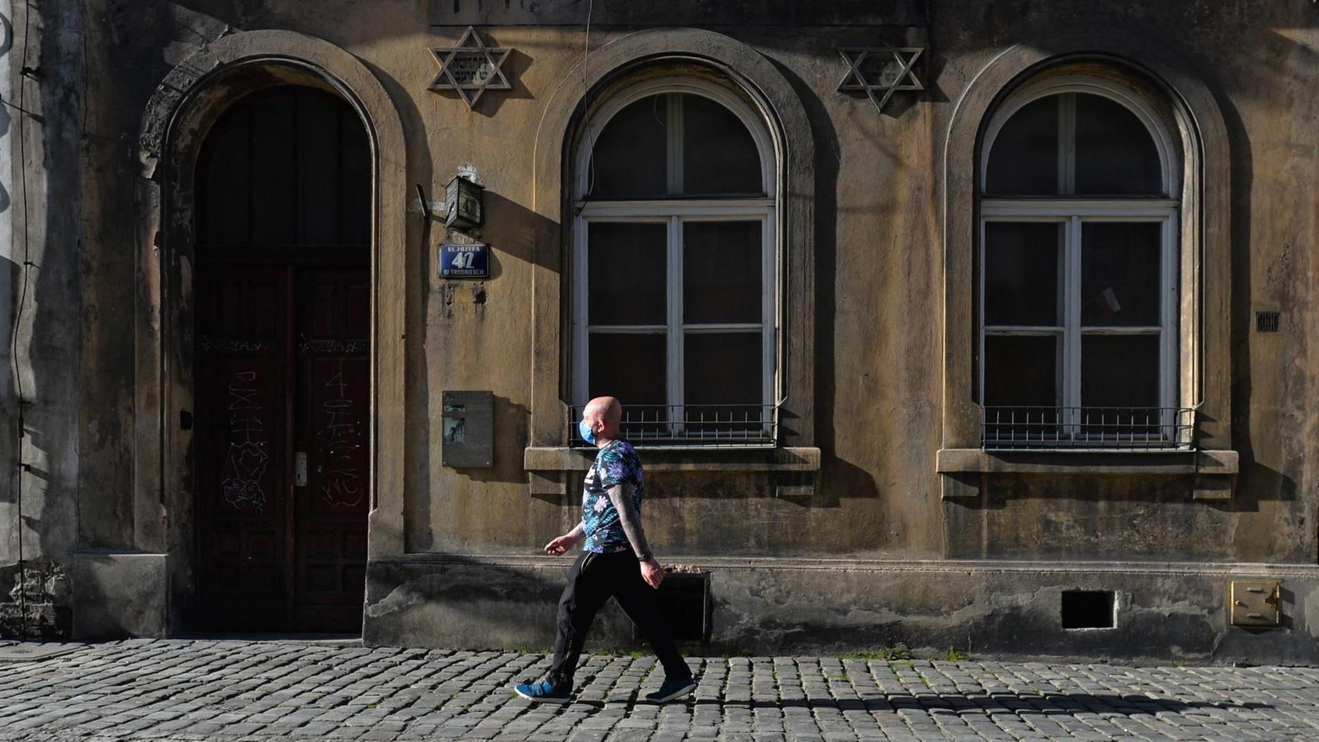 Ein Passant mit Schutzmaske geht an einem alten Gebäude mit Davidsternen an der Fassade vorbei. Ein Passant mit Schutzmaske geht an einem alten Gebäude mit Davidsternen an der Fassade vorbei.