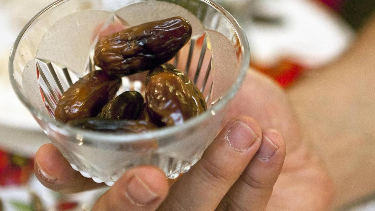 Eine Hand hält ein Glasschälchen mit Datteln. Eine Hand hält ein Glasschälchen mit Datteln.