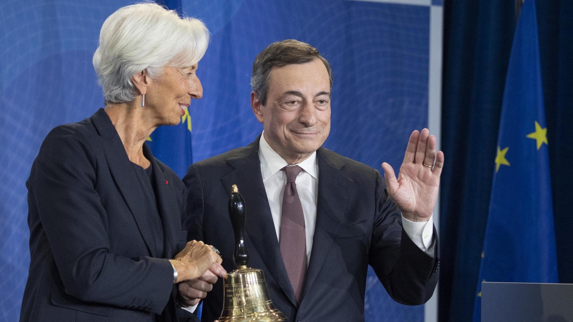 Lagarde drückt eine Hand Draghis. Dieser winkt. Er übergibt ihr die Sitzungsglocke. Lagarde drückt eine Hand Draghis. Dieser winkt. Er übergibt ihr die Sitzungsglocke.