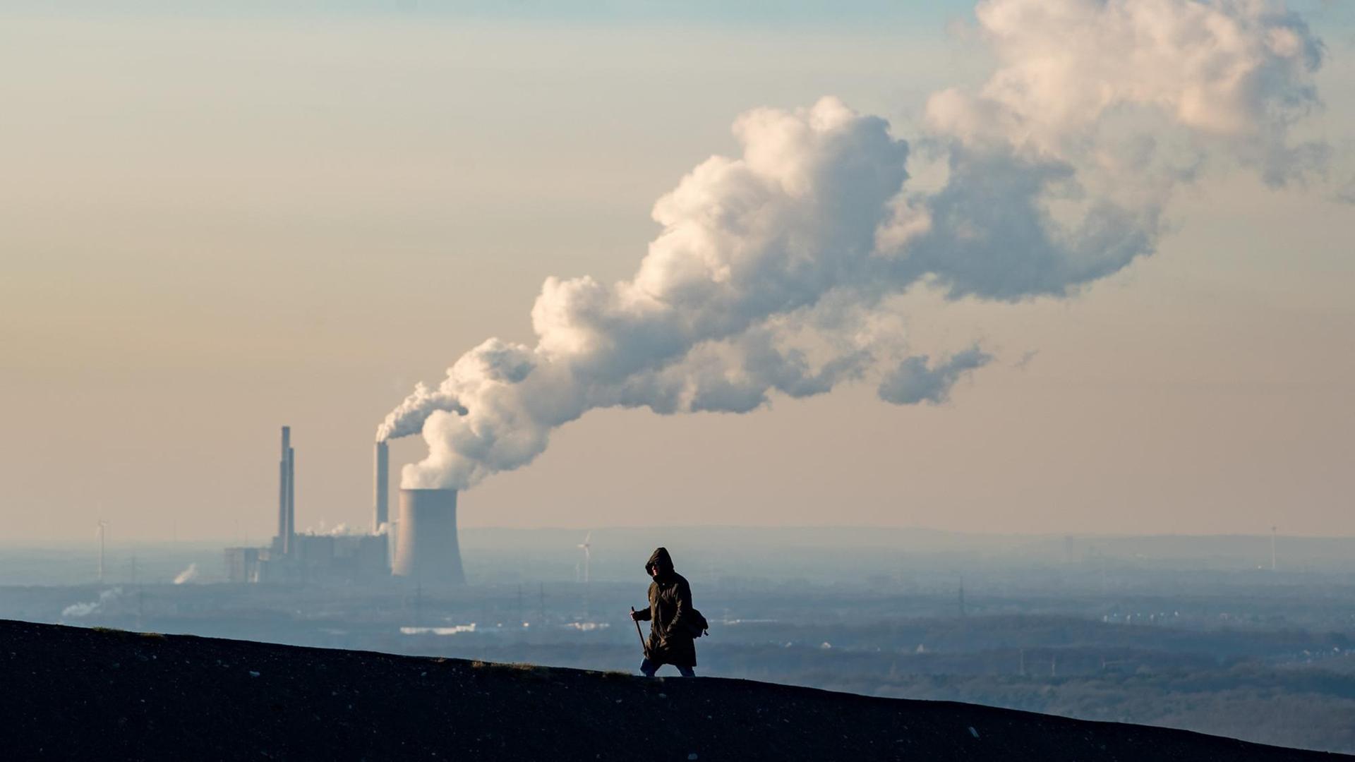 Rauch und Dampf steigen aus einem Kohlekraftweg in Oberhausen auf, im Vordergrund geht ein Mann.