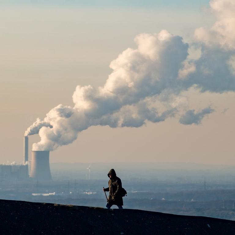 Rauch und Dampf steigen aus einem Kohlekraftweg in Oberhausen auf, im Vordergrund geht ein Mann.
