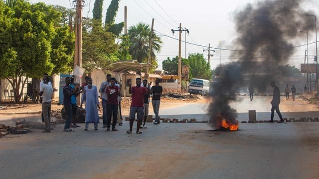 Auf einer Straße in der sudanesischen Hauptstadt Khartoum demonstrieren Menschen neben einem brennenden Autoreifen. 