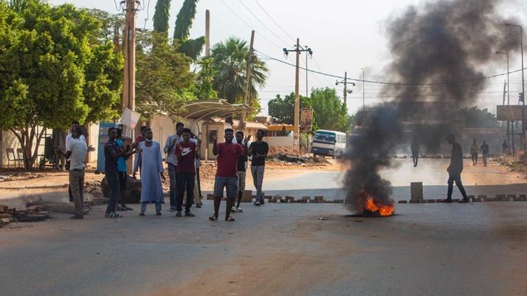 Auf einer Straße in der sudanesischen Hauptstadt Khartoum demonstrieren Menschen neben einem brennenden Autoreifen. Auf einer Straße in der sudanesischen Hauptstadt Khartoum demonstrieren Menschen neben einem brennenden Autoreifen.
