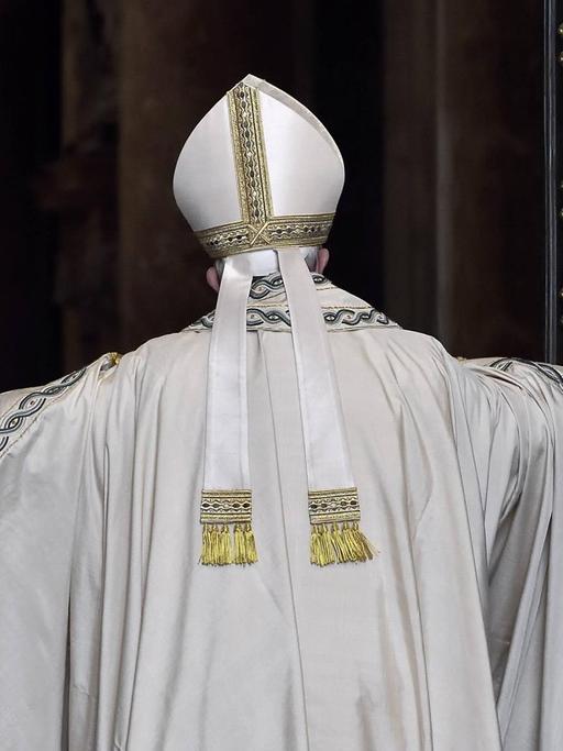 Papst Franziskus von Hinten, wie er die großen Flügel der "Heiligen Pforte" öffnet. Das Portal besteht aus zwei großen Kassettentüren mit schwarzen Rahmen und goldenen Kassetten mit Motiven der Heilsgeschichte.