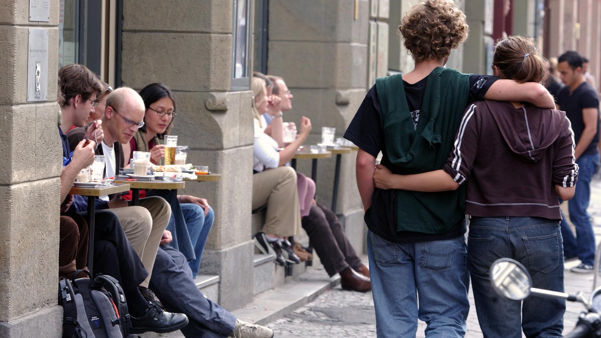 Ein junges Paar flaniert in Berlin-Mitte an einem Café vorbei. Ein junges Paar flaniert in Berlin-Mitte an einem Café vorbei.