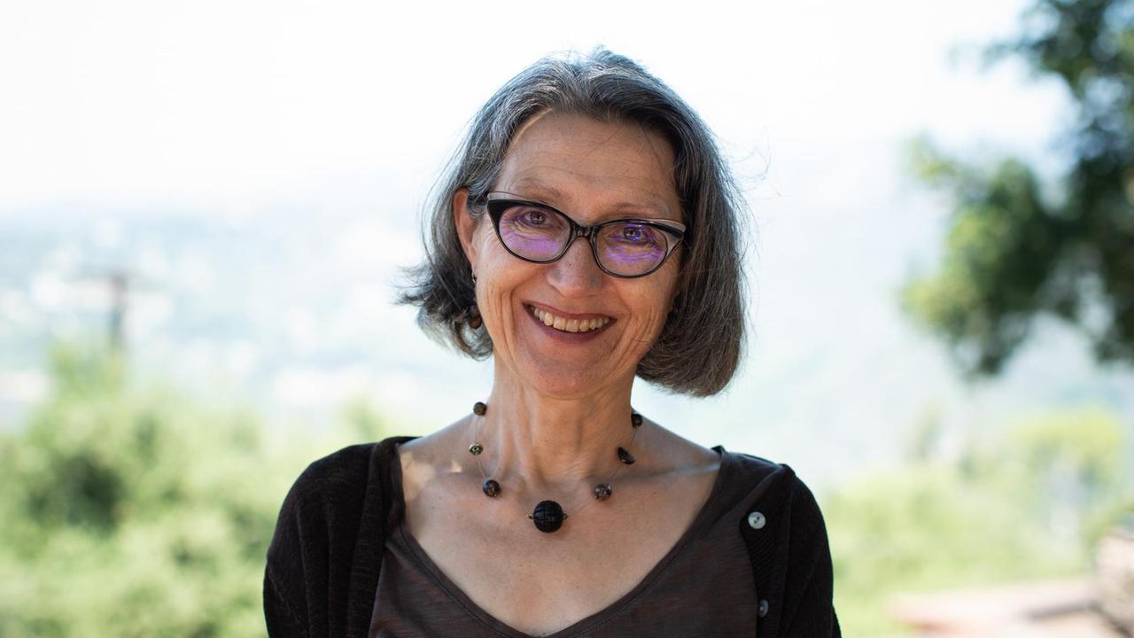 Eine ältere lächelnde Dame mit dunkelumrandeter Brille und auffälliger Halskette. Eine ältere lächelnde Dame mit dunkelumrandeter Brille und auffälliger Halskette.