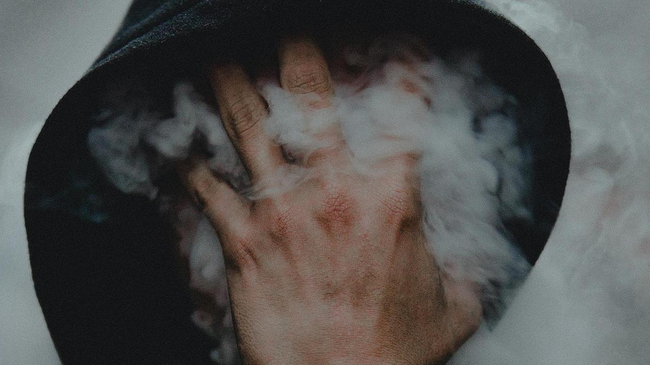 Ein Mann pustet Dampf gegen seine Hand, die er vor sein Gesicht hält. Dadurch legt sich der Dampf nebelartig vor sein Gesicht. Ein Mann pustet Dampf gegen seine Hand, die er vor sein Gesicht hält. Dadurch legt sich der Dampf nebelartig vor sein Gesicht.