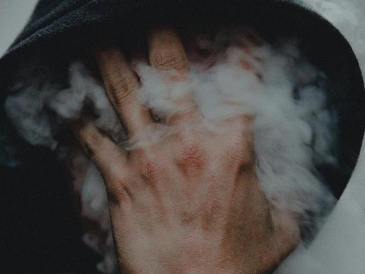 Ein Mann pustet Dampf gegen seine Hand, die er vor sein Gesicht hält. Dadurch legt sich der Dampf nebelartig vor sein Gesicht.