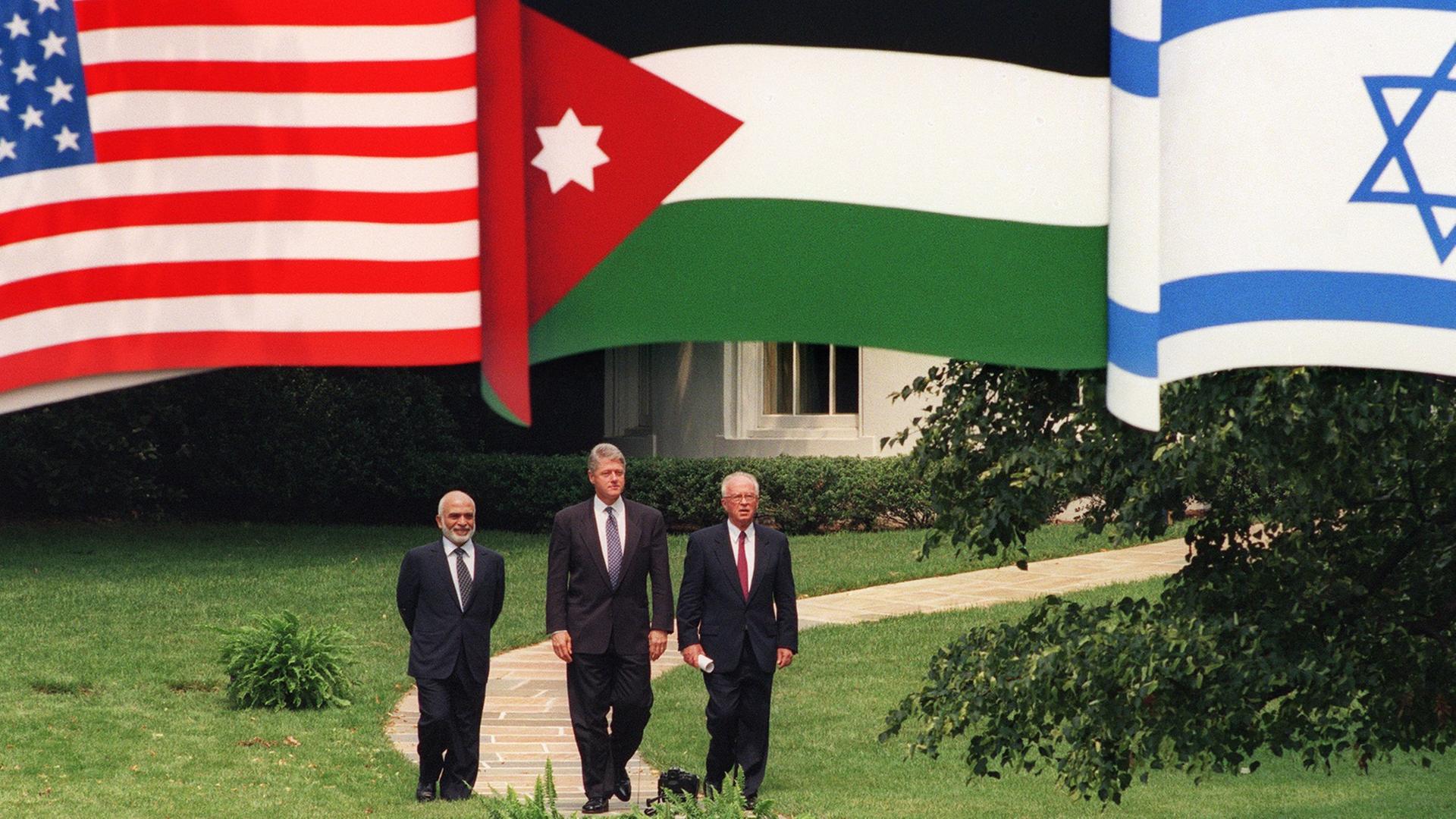 US-Präsident Bill Clinton (Mitte) mit Jordaniens König Hussein (links) und Israels Premier Yitzhak Rabin laufen einen Weg entlang, darüber hängen die Fahnen der drei Länder. US-Präsident Bill Clinton (Mitte) mit Jordaniens König Hussein (links) und Israels Premier Yitzhak Rabin laufen einen Weg entlang, darüber hängen die Fahnen der drei Länder.