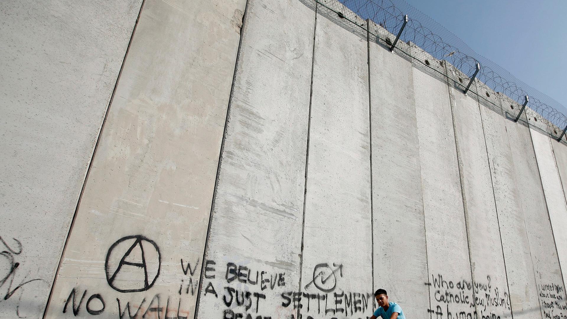 Ein arabischer Junge fährt im Osten Jerusalems auf einem Rad am Trennwall zwischen Israel und dem palästinensischen Gebiet entlang. Ein arabischer Junge fährt im Osten Jerusalems auf einem Rad am Trennwall zwischen Israel und dem palästinensischen Gebiet entlang.