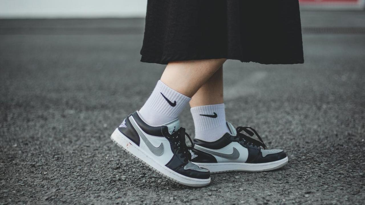 Beine in Rock, Sportsocken und Sneakers auf Asphalt Beine in Rock, Sportsocken und Sneakers auf Asphalt
